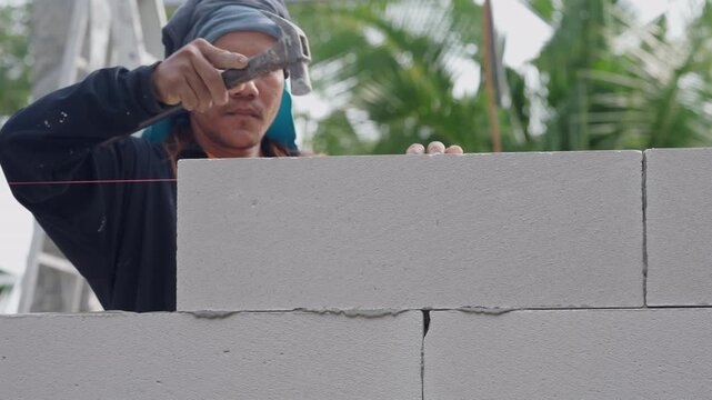 Builder installing concrete block with fresh mortar during industrial construction process. Closeup detail showing professional skill and wall structure development outdoors.
