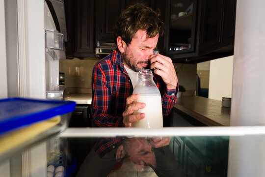 Man reacting to bad smell from spoiled milk in fridge, pinching his nose with disgusted face