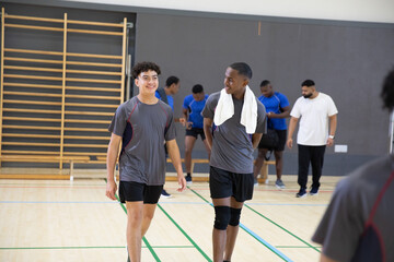 Teenage male athletes walking and talking in school gym in sportswear, wearing towel and knee-pad