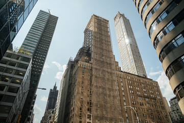 A mix of old and new architecture stands tall in Midtown Manhattan. One historic building is under renovation with scaffolding surrounding its facade.