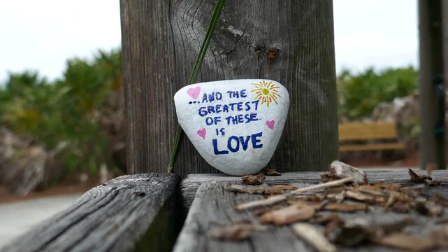 And the greatest of these is love kindness rock on wooden boards with nature debris falling around