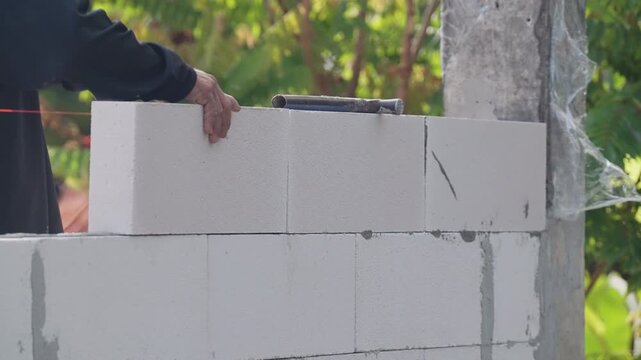 Detailed closeup of concrete block wall construction using mortar and trowel. Industrial building process highlighting structural strength, precision alignment and professional workmanship.