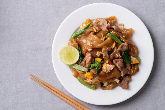 Top view of Thai food (Pad See Ew), Stir-fried rice noodles with soy sauce, pork, egg, and kale on a white plate with chopsticks