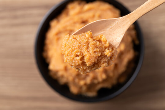 Close up of scooping traditional Japanese miso paste from a black bowl with a wooden spoon, fermented soybean seasoning for cooking