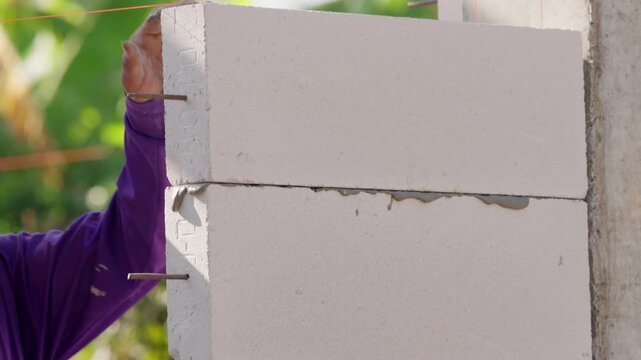 Detailed closeup of concrete block wall installation with mortar for structural engineering project. Industrial construction process highlighting strength, alignment and durability.