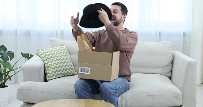 Happy man taking hat from open parcel on sofa at home