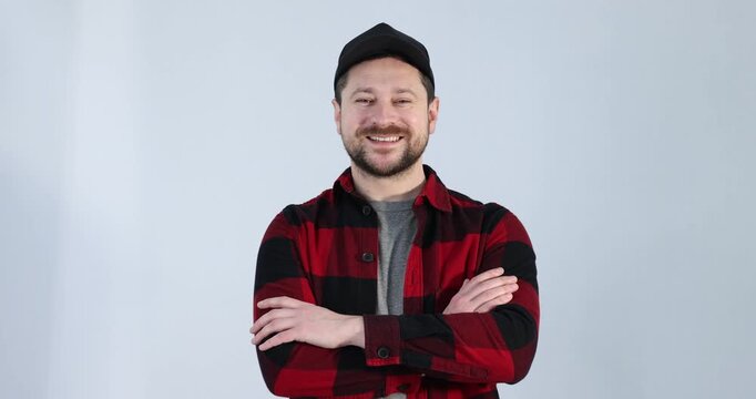 Smiling long-haul truck driver in baseball cap and red checkered shirt posing with crossed arms on grey background