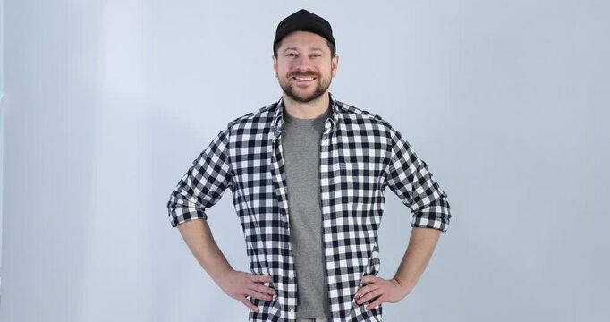 Smiling long-haul truck driver in baseball cap and checkered shirt posing on grey background