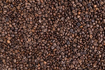 Top view of roasted coffee beans scattered to create a dense, seamless texture. Full frame flat lay background with copy space. Concept of morning boost, specialty cafe, roastery