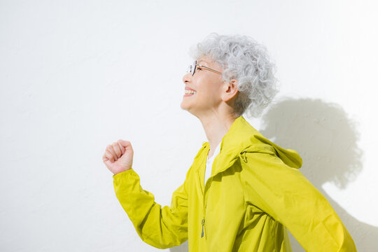 スポーツウェアで走るポーズをするお洒落なグレイヘアのアクティブシニアの眼鏡の女性　見上げる横顔クローズアップ