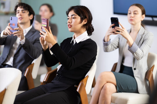 Young woman scans QR codes or takes photo of presentation using smartphone during meeting in office