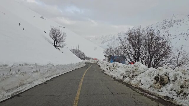 a narrow winding mountain road lined with snowbanks and bare winter trees, leading through a quiet snowy landscape under an overcast sky.  
📍Hawraman Takht, Kurdistan 