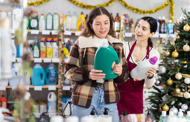 Obraz premium In X mas atmosphere, girl consultant helps female buyer choose laundry softener, answers questions and accompanies during shopping, recommended some item. .