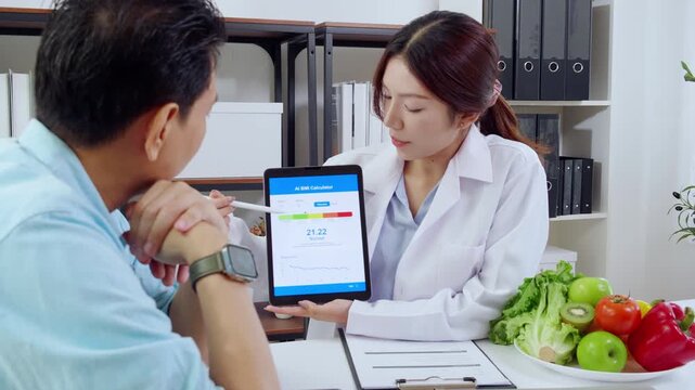 Asian woman nutritionist showing AI BMI calculator on tablet and explaining to man patient, doctor using digital health technology for medical diagnosis, wellness planning and weight control.
