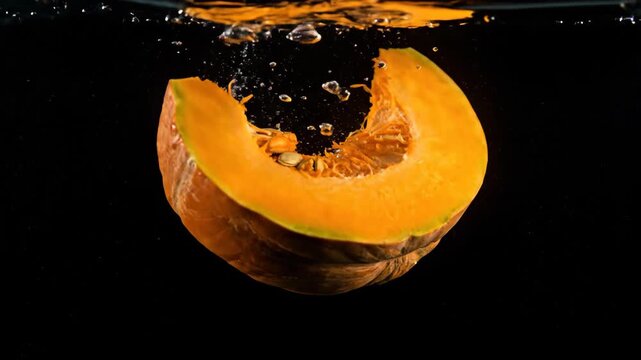 Fresh pumpkin slice falling into water on black backdrop, orange fruit, food.