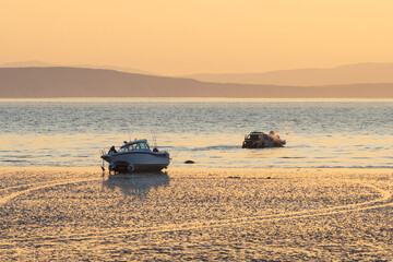 Boat on the shallows at low tide. An off-road car takes a boat into the water. Preparation for fishing. Morning seascape at sunrise. View of the shallows and the sea bay. Golden morning sunlight.