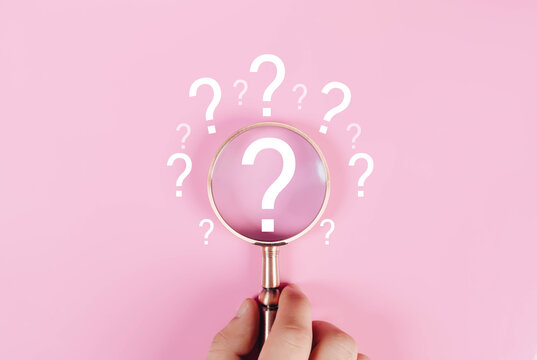 Magnifying glass focusing on question mark icons over pink background. Search concept, problem solving, FAQ support, investigation, curiosity and information discovery in digital marketing.