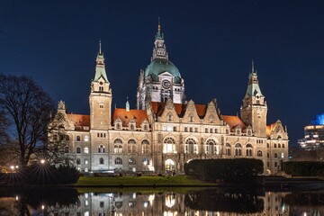 Discover the enchanting night view of Hannover, Germany, featuring the illuminated New Town Hall reflected in the serene pond. A stunning showcase of Hannover s architectural beauty.