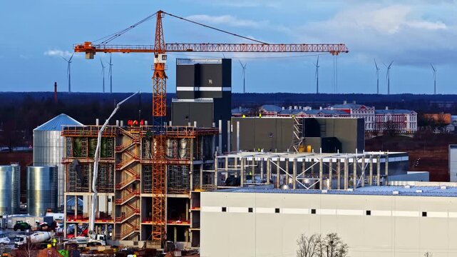 Construction Crane Towers Over Building Under Development At Industrial Site. ascending drone shot