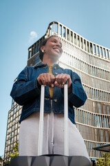 Young black woman smiling with luggage in front of modern building