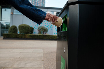 Person throwing paper cup in recycling bin promoting environmental awareness