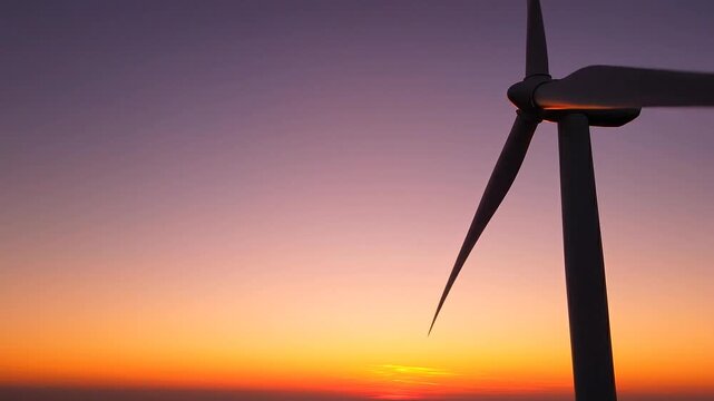 Silhouette of a Wind Turbine Rotating Against a Vibrant Sunset Sky with Orange and Purple Hues