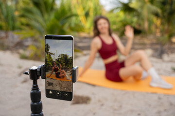 Woman recording online fitness workout on smartphone in tropical outdoor setting