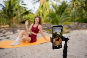 Woman recording fitness workout on smartphone outdoors in tropical setting