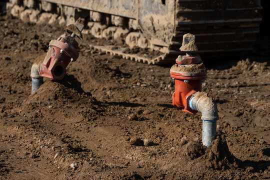Newly installed water utility pipeline and backflow preventer in fresh dirt on development construction job site, tracked heavy equipment vehicle I background
