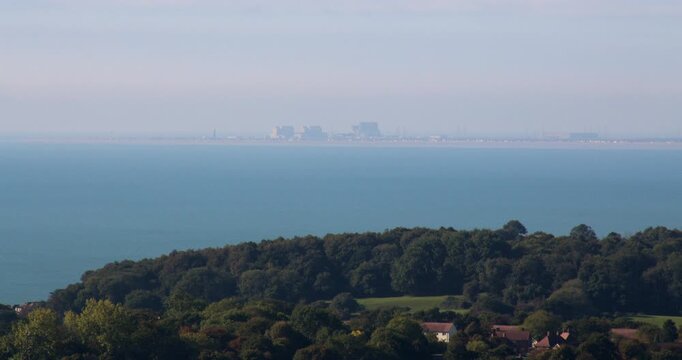 Distant shot of Dungeness Power Station Nuclear power plant with wooded hill in foreground.