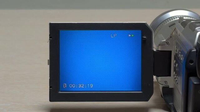 A vintage camcorder begins fast-forwarding through a tape. The internal gears spin rapidly, producing an anxious, high-pitched mechanical whir. This sharp sound echoes as the timestamp advances.