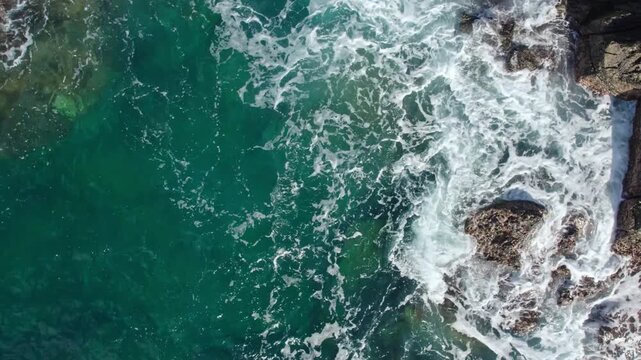 Drone pedestal shot moving up slowly over concrete wave breakers as ocean waves splash. Industrial coastal protection and water foam from above.