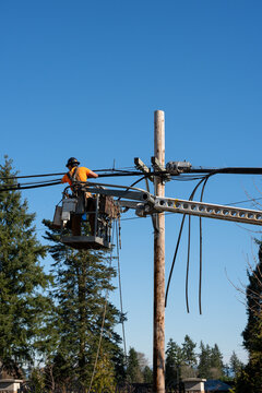 Power utility lineman in an aerial lift bucket using a Cable Lasher to upgrade utilities by replacing power lines and communication cable with fiber optics
