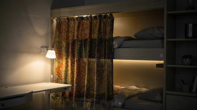 Softfocus shelving and a glowing reading light frame a dorm bunk bed with vibrant patterned curtains drawing attention to the privacy fabric in sharp focus.
