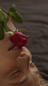 Sensual vertical close up of a rose teasingly caressing the face of a beautiful blonde woman