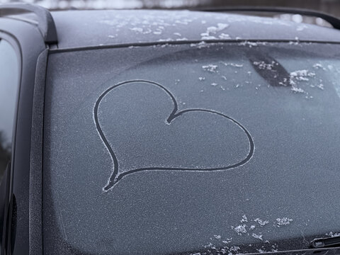 Valentine's Day concept: hand-drawn heart pattern on a frozen car windshield. Hand drawn heart shape on windshield of the car. Love symbol. Romantic background. A frozen windshield with a heart.