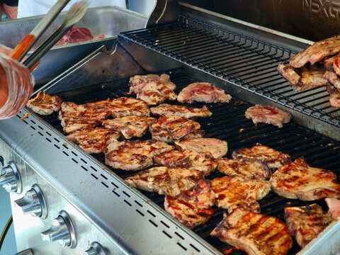 Juicy pork chops searing beautifully on a large outdoor stainless steel barbecue grill during cooking