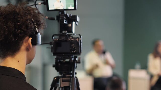 Professional video camera on tripod filming speaker during conference or public event indoors.