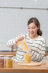 Young woman decanting cereal into a reusable glass jar in a bright kitchen. Concept of pantry organization, sustainable living, and zero waste lifestyle.