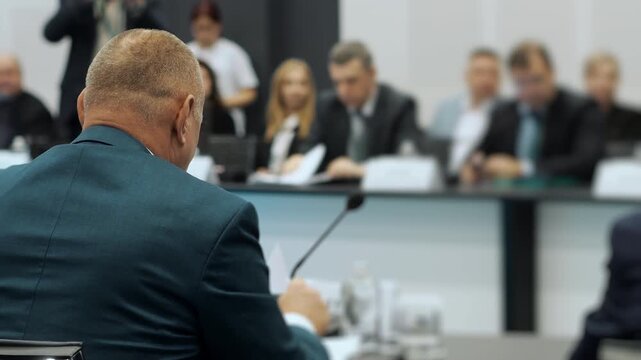 Mature businessman in suit speaking at formal board meeting in modern conference room, corporate leadership discussion and decision making indoors.
