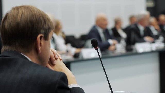 Business meeting or conference discussion with microphone in foreground and group of participants in background indoors.