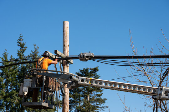 Power utility lineman in an aerial lift bucket using a Cable Lasher to upgrade utilities by replacing power lines and communication cable with fiber optics

