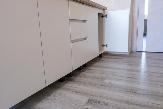 Modern kitchen base cabinet with white minimalist drawers and an open cupboard door on new grey laminate flooring