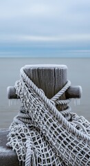 Fototapeta premium Frozen dock post wrapped in frosty rope and netting by a icy winter lake with overcast sky