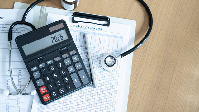Top view of annual health check checklist with stethoscope and calculator on wooden desk, concept of medical examination planning, healthcare cost and preventive routine checkup.