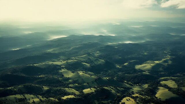 Layering mountains and valleys stretching into the distance under a dramatic sky, featuring sun rays breaking through clouds and creating misty atmospheric conditions over the landscape