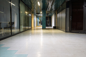 Obraz premium Empty Abandoned City Hall Building Corridor With Long Hallway, Glass Partition Walls, Teal Ceiling Panels, White Tiled Floor, And Atmospheric Fluorescent Lighting In A Vacant Historic Civic Space