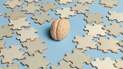 Human Brain Model Surrounded by Wooden Jigsaw Puzzle Pieces on Blue Background