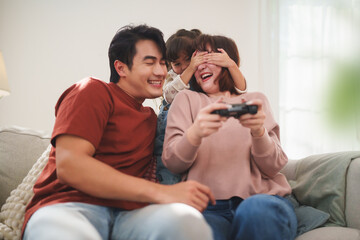 Happy Asian family playing console game together on sofa at home