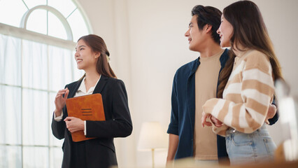 Asian female real estate agent showing house tour with tablet to young couple